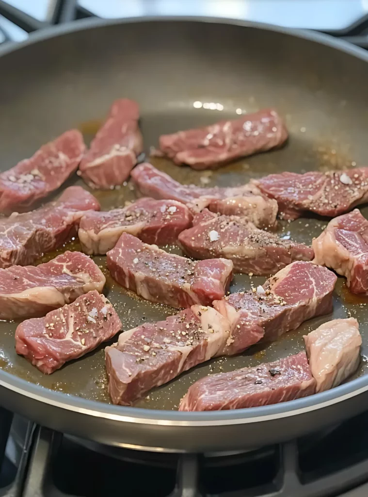 Beef strips searing in skillet with seasoning