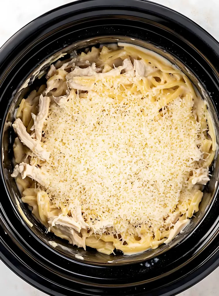 Chicken and pasta topped with grated cheese in crockpot