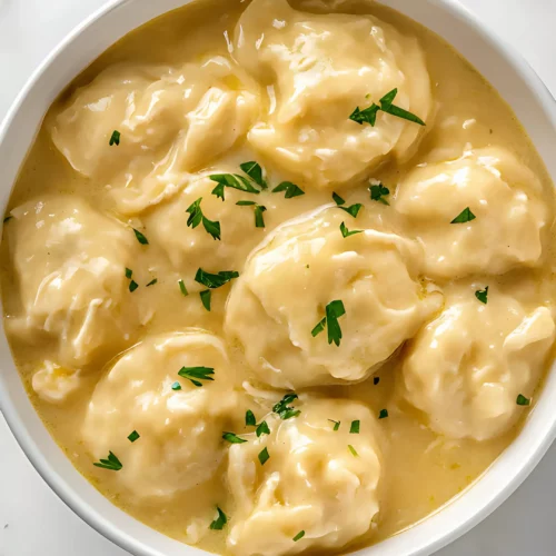 Creamy chicken and dumplings topped with fresh parsley in a white bowl