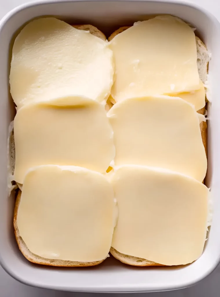 Provolone cheese slices on slider buns in a white baking dish