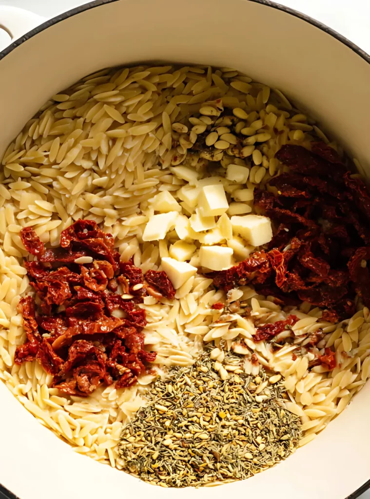 Uncooked orzo pasta with sun-dried tomatoes and herbs in a pot