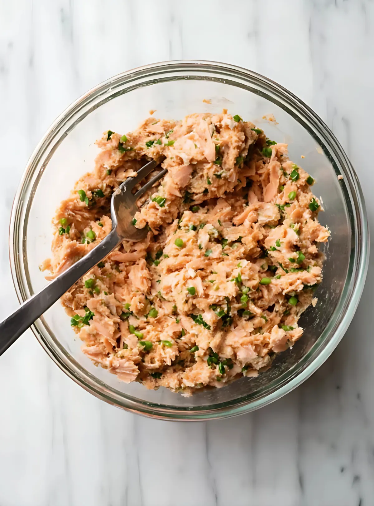 Flaked salmon mixed with herbs and breadcrumbs in prep bowl with fork