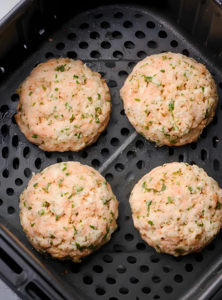 Raw salmon patties in air fryer basket before cooking