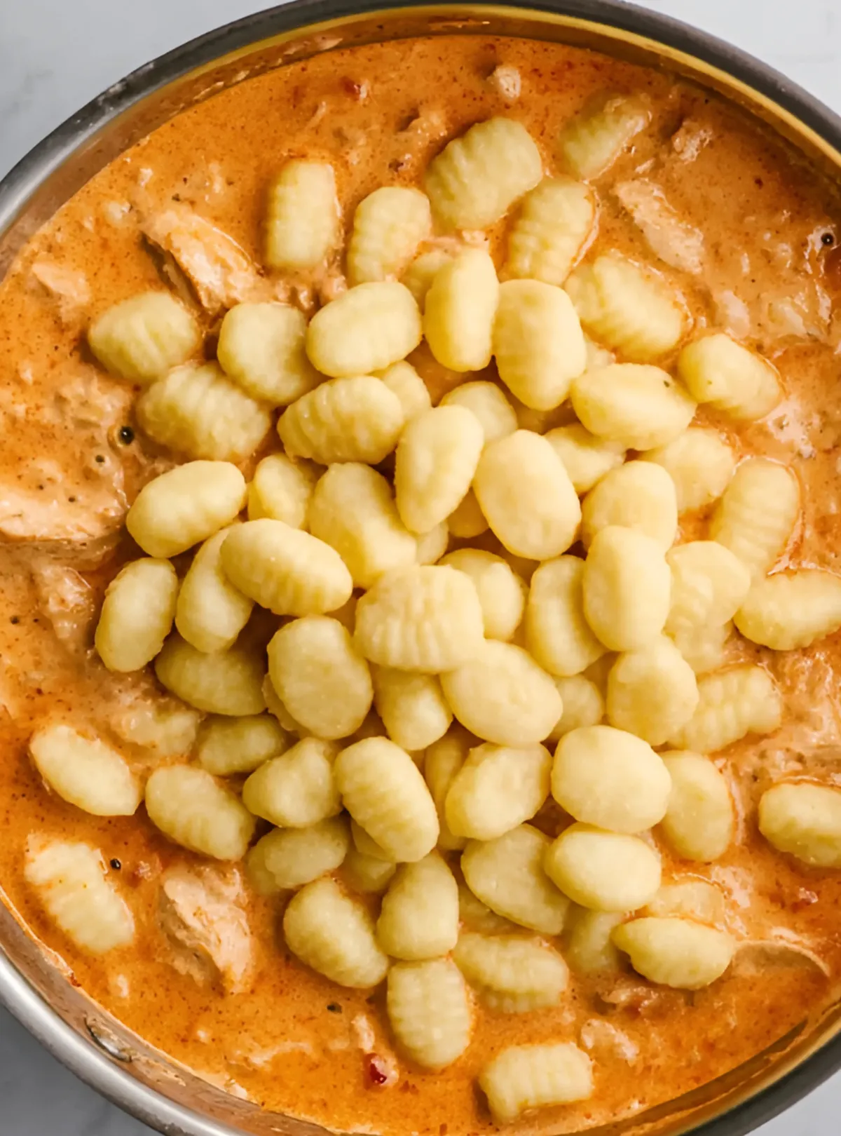 Uncooked gnocchi in creamy sauce in skillet
