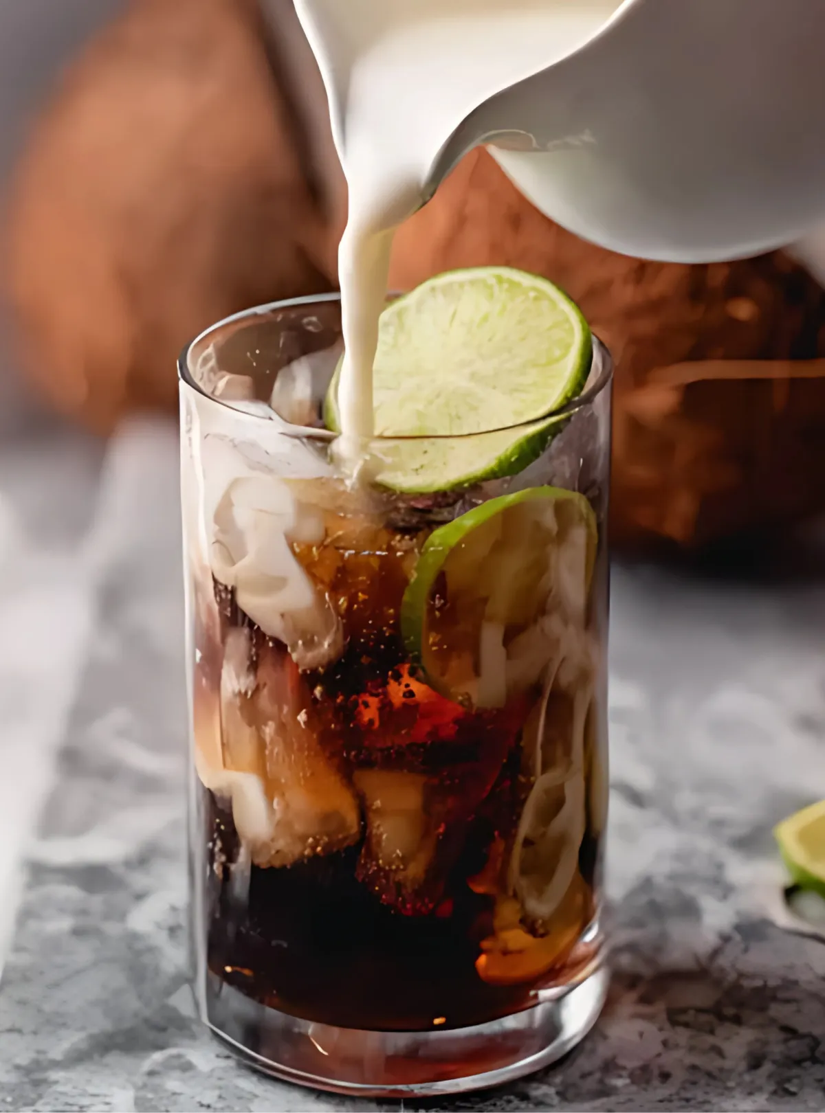 Cream being poured into dark soda with lime and coconut around