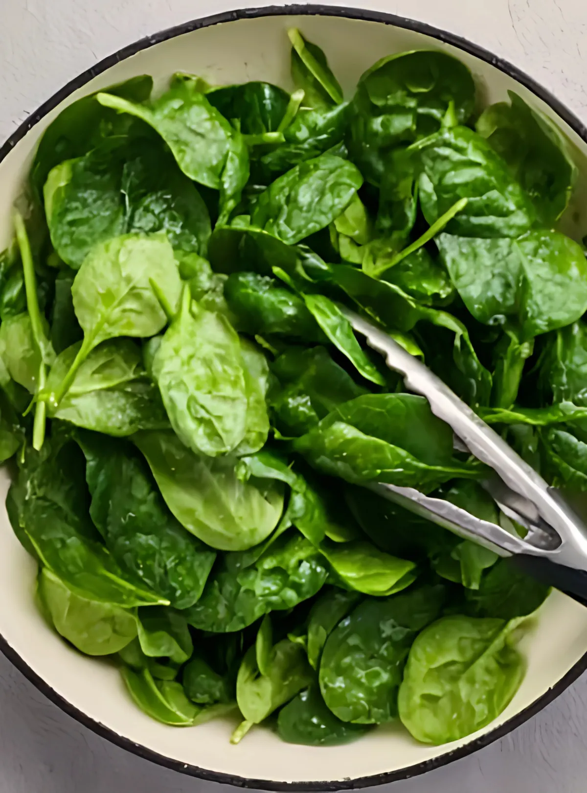Fresh baby spinach in skillet with tongs