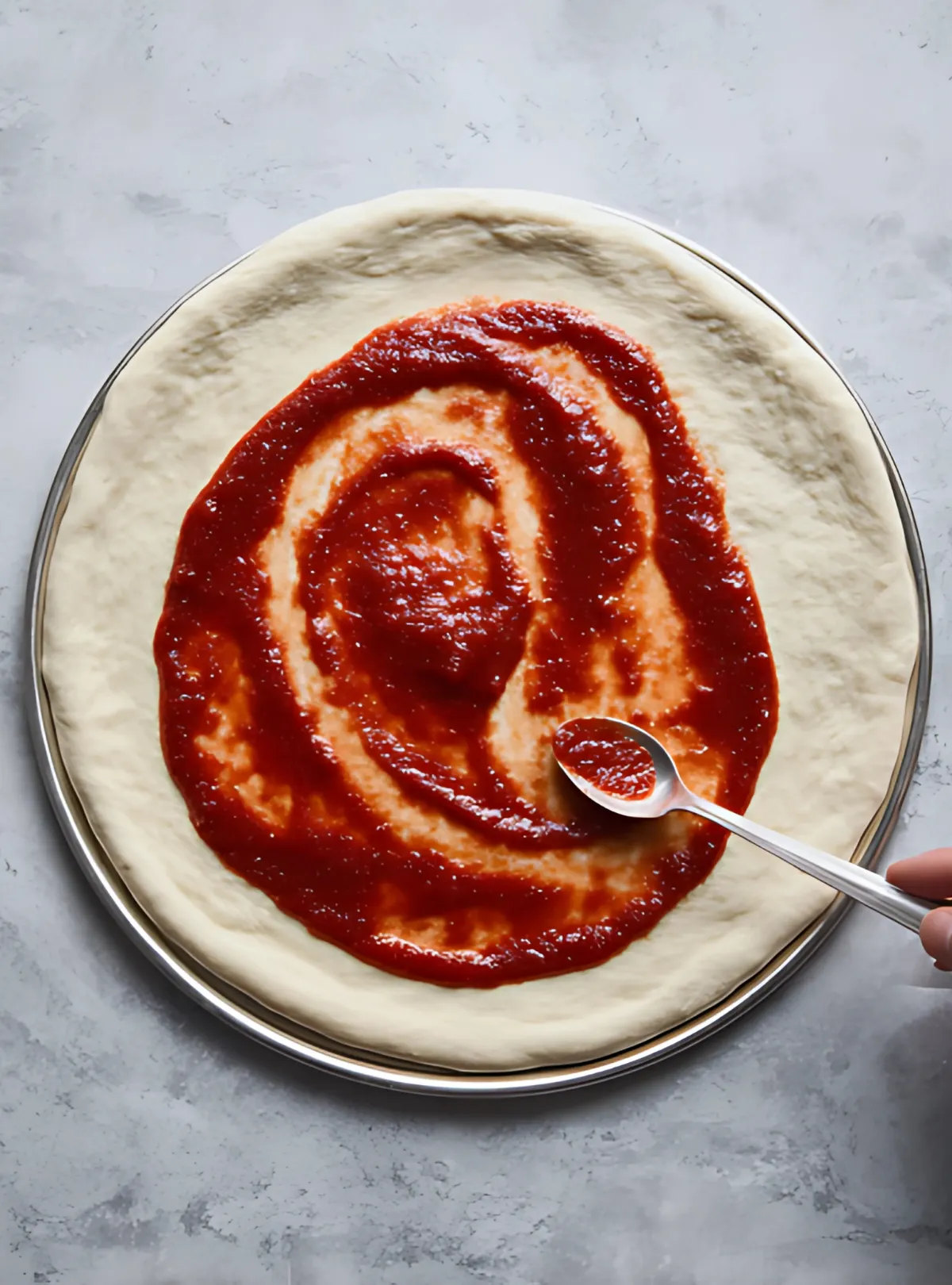 Pizza dough with sauce spread by spoon