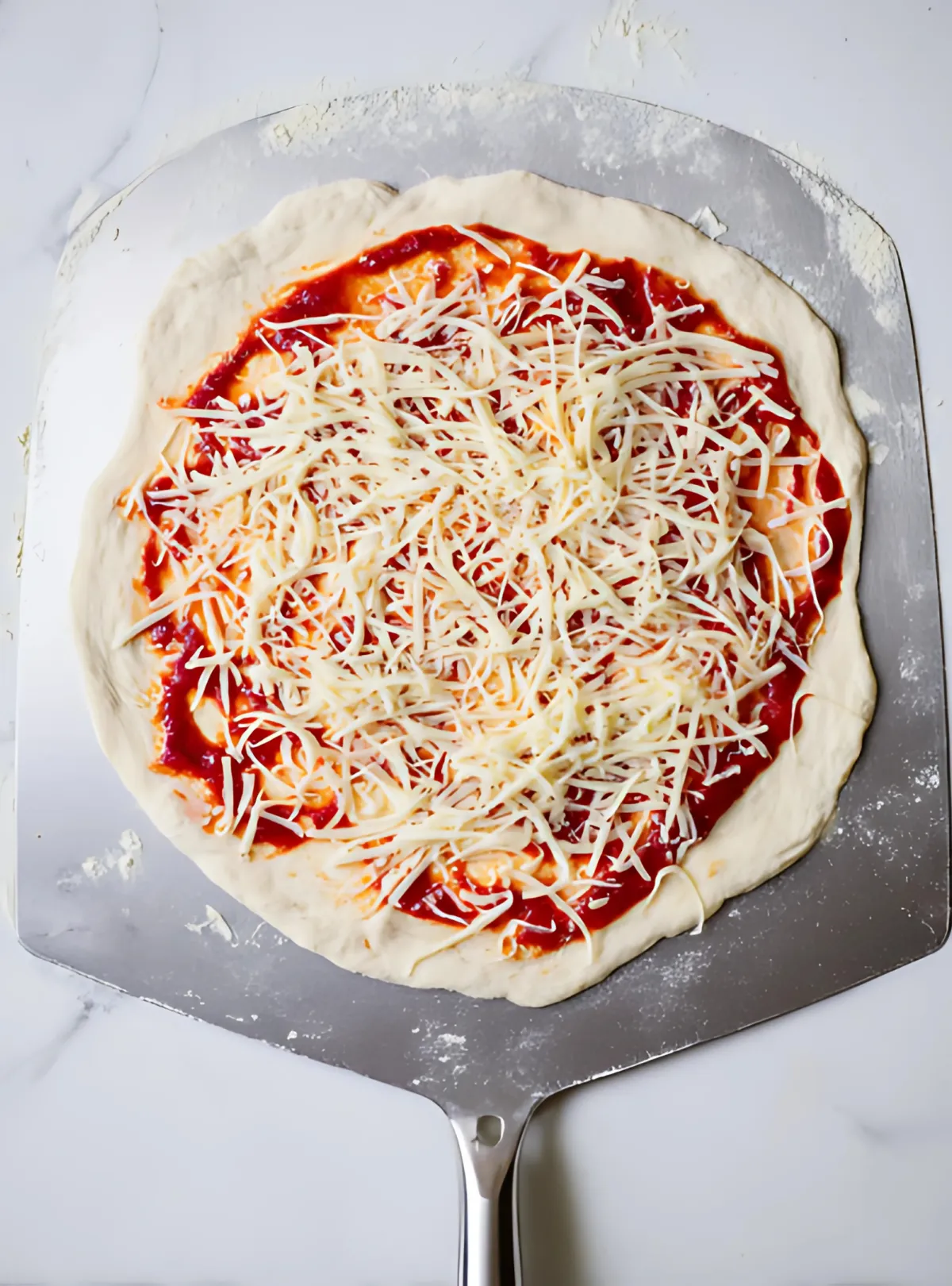 Raw pizza on metal peel with cheese