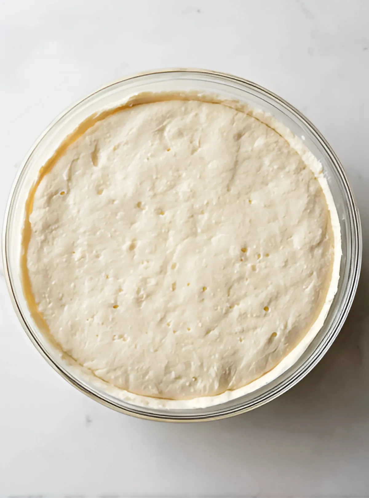 Risen dough in clear glass bowl