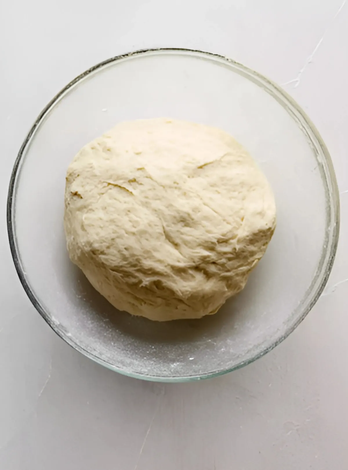 Smooth ball of pizza dough in glass bowl
