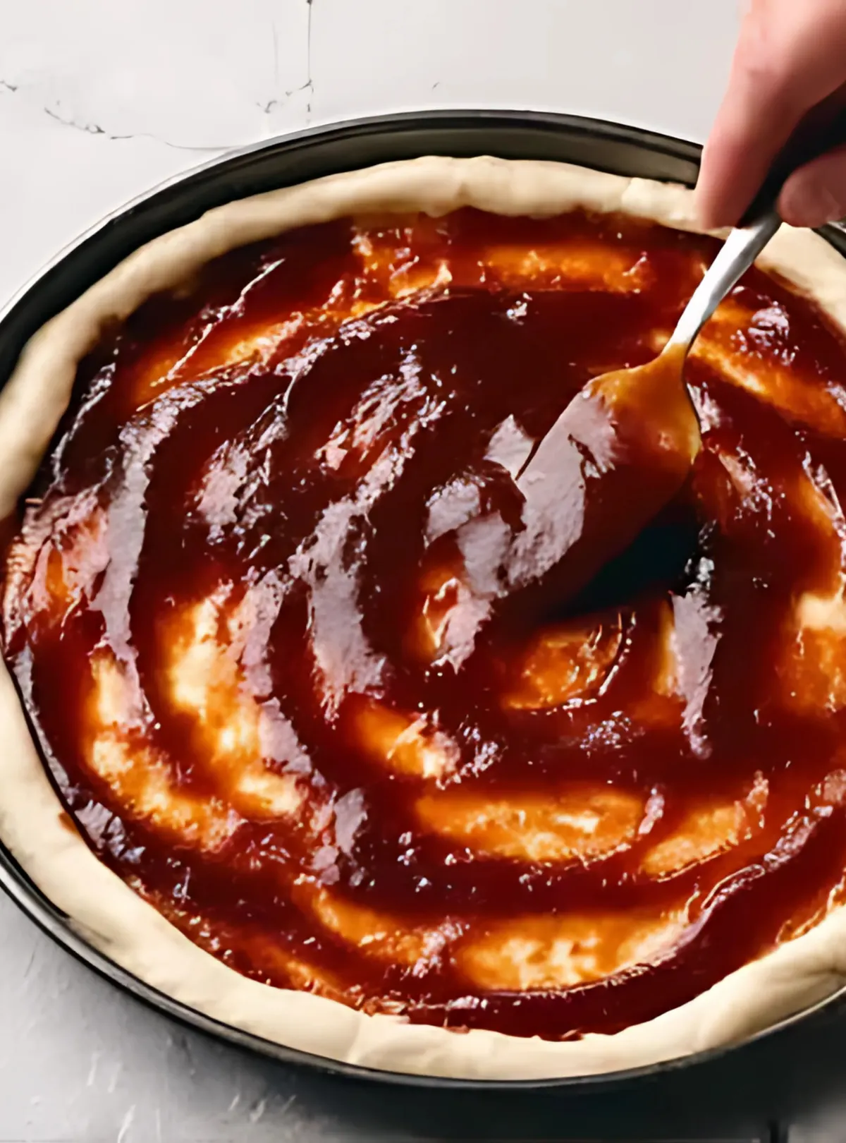 Spreading barbecue sauce on raw dough