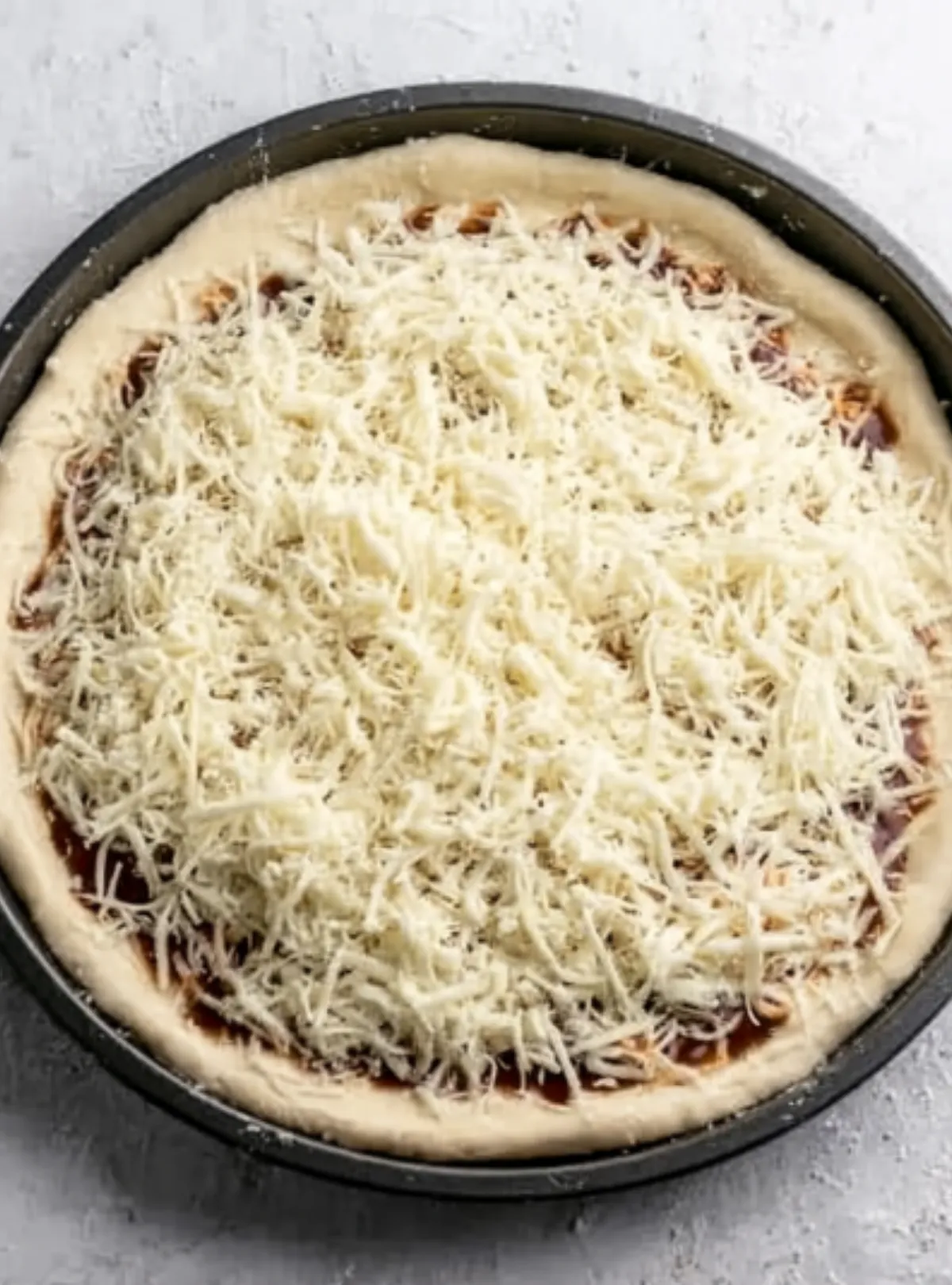 Unbaked pizza topped with shredded cheese
