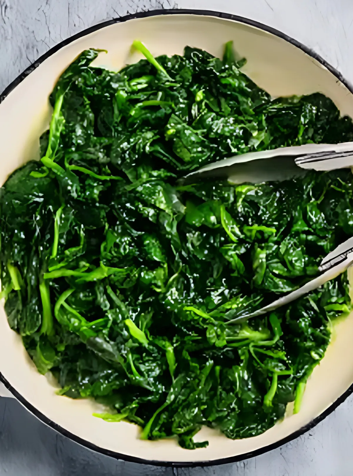 Wilted spinach in skillet with tongs