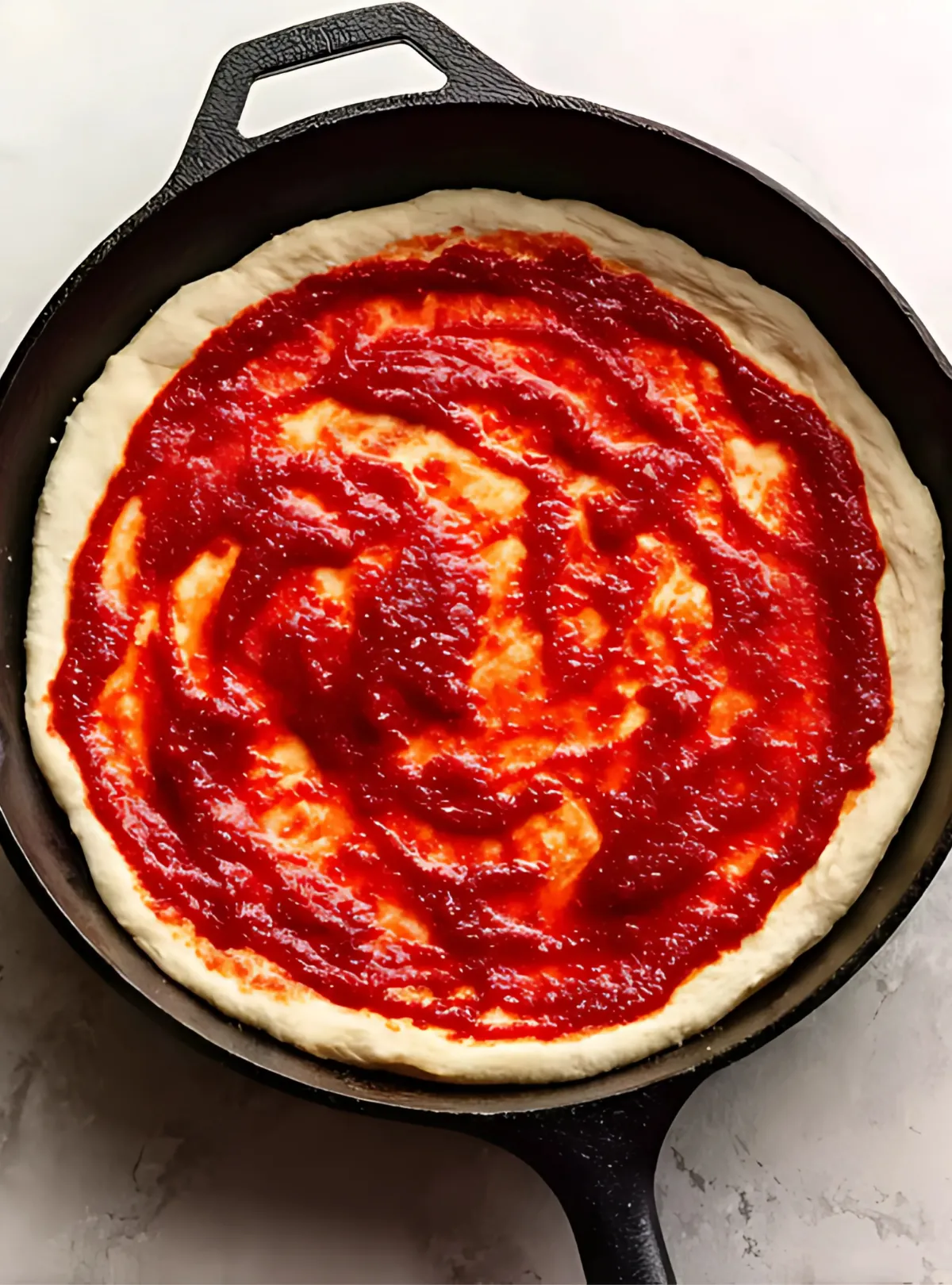 pizza dough with sauce in cast iron pan