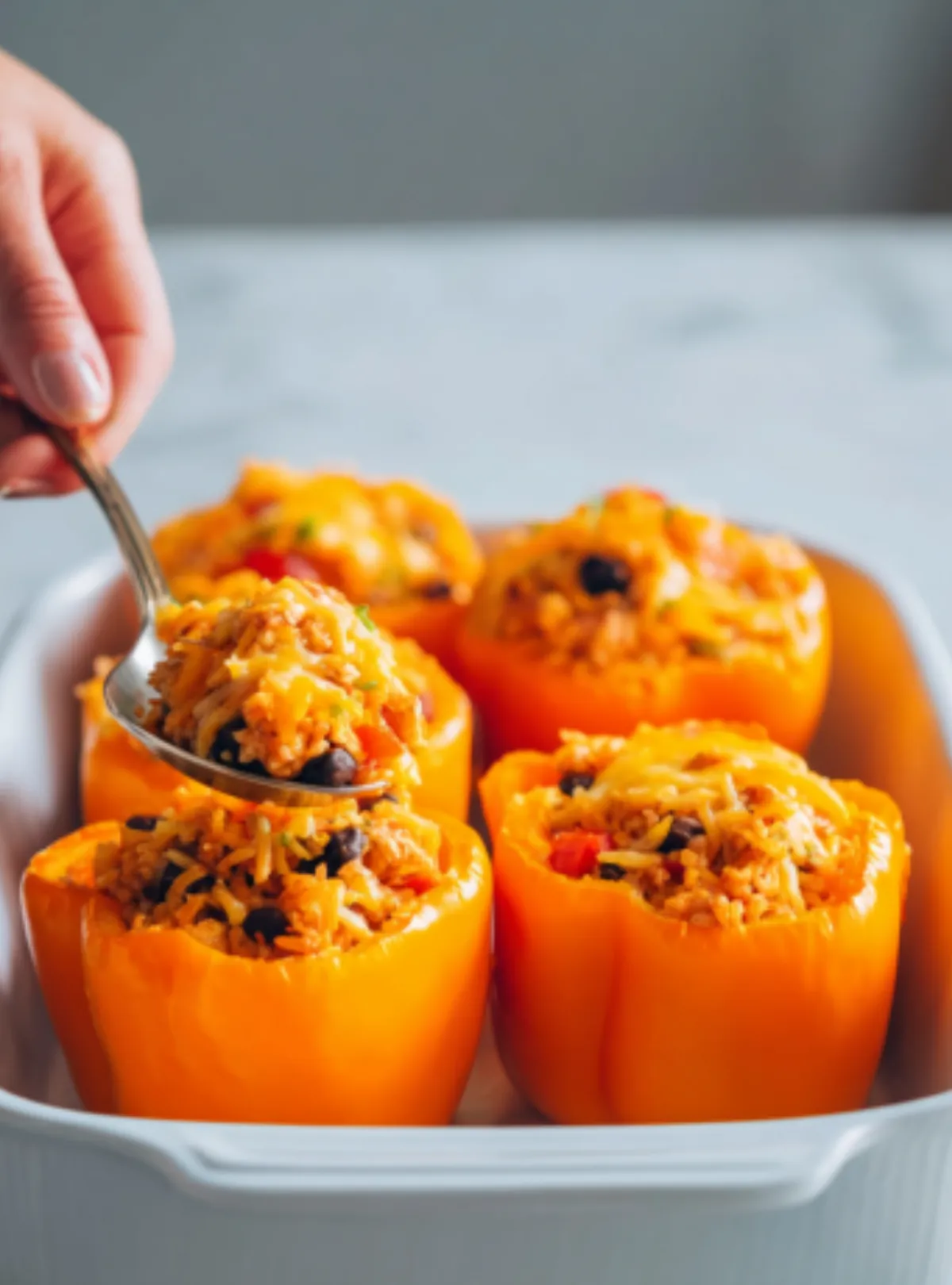 Hand spooning filling into orange peppers in baking dish