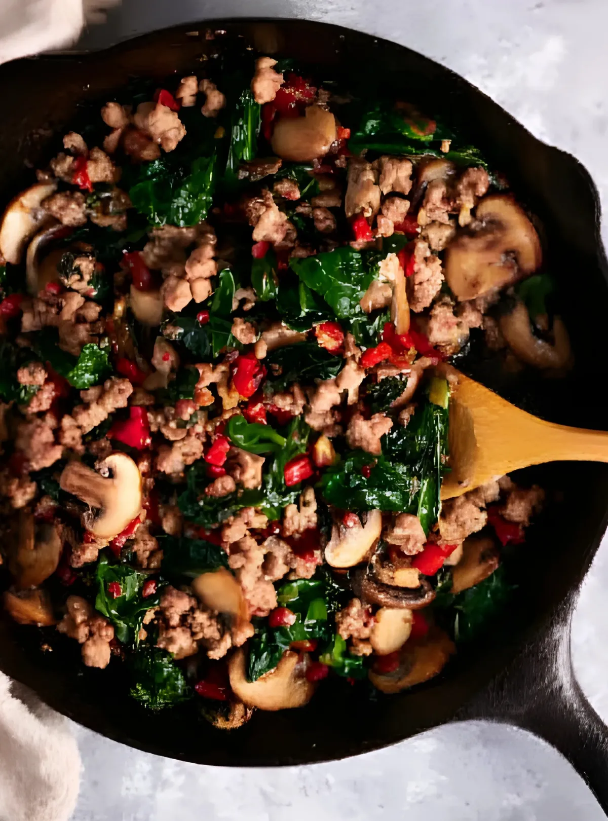 Sausage spinach mushroom mix in skillet with spoon