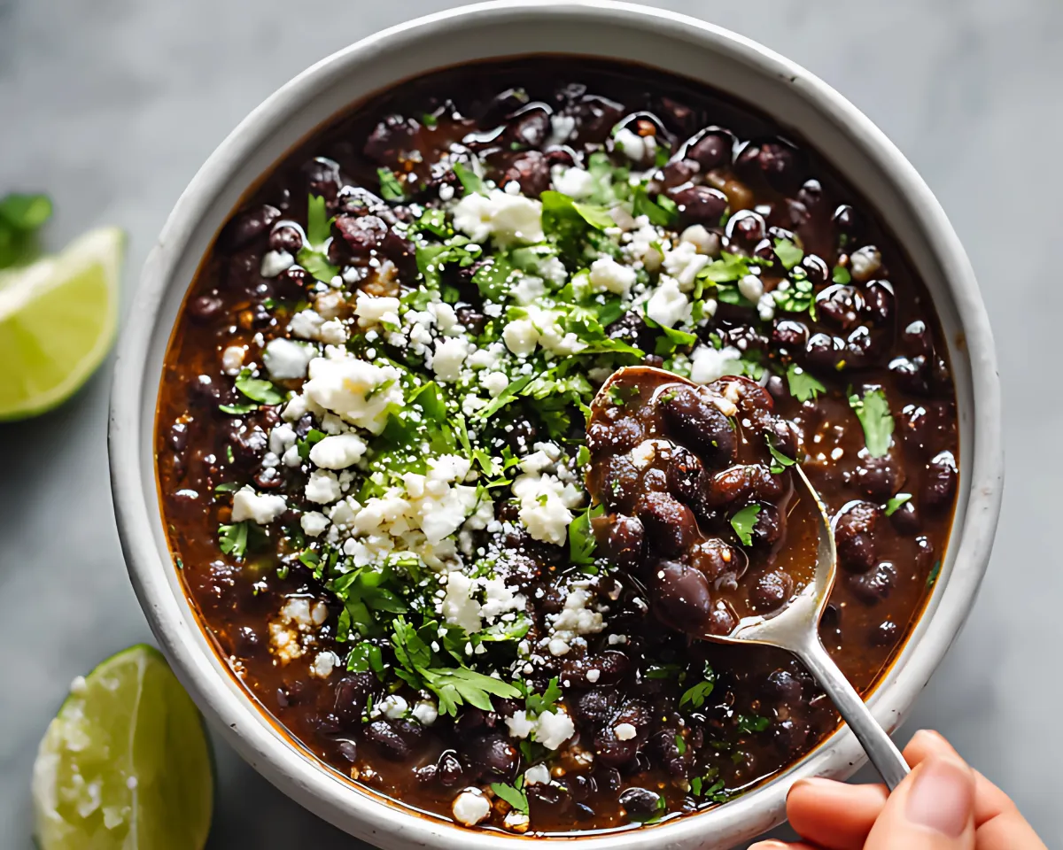 hand holding spoon over garnished black beans in bowl