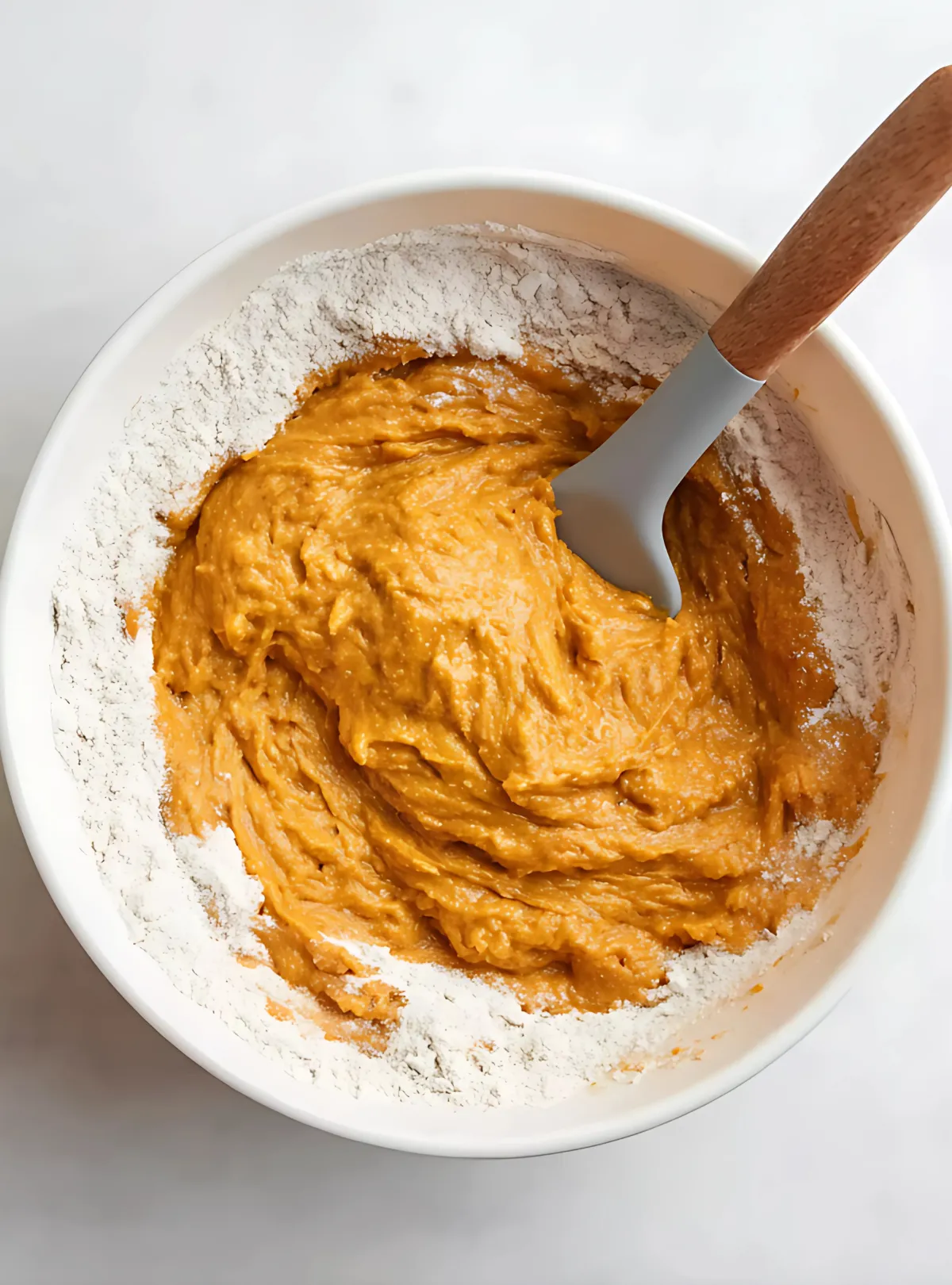 Orange donut batter being mixed with flour in bowl