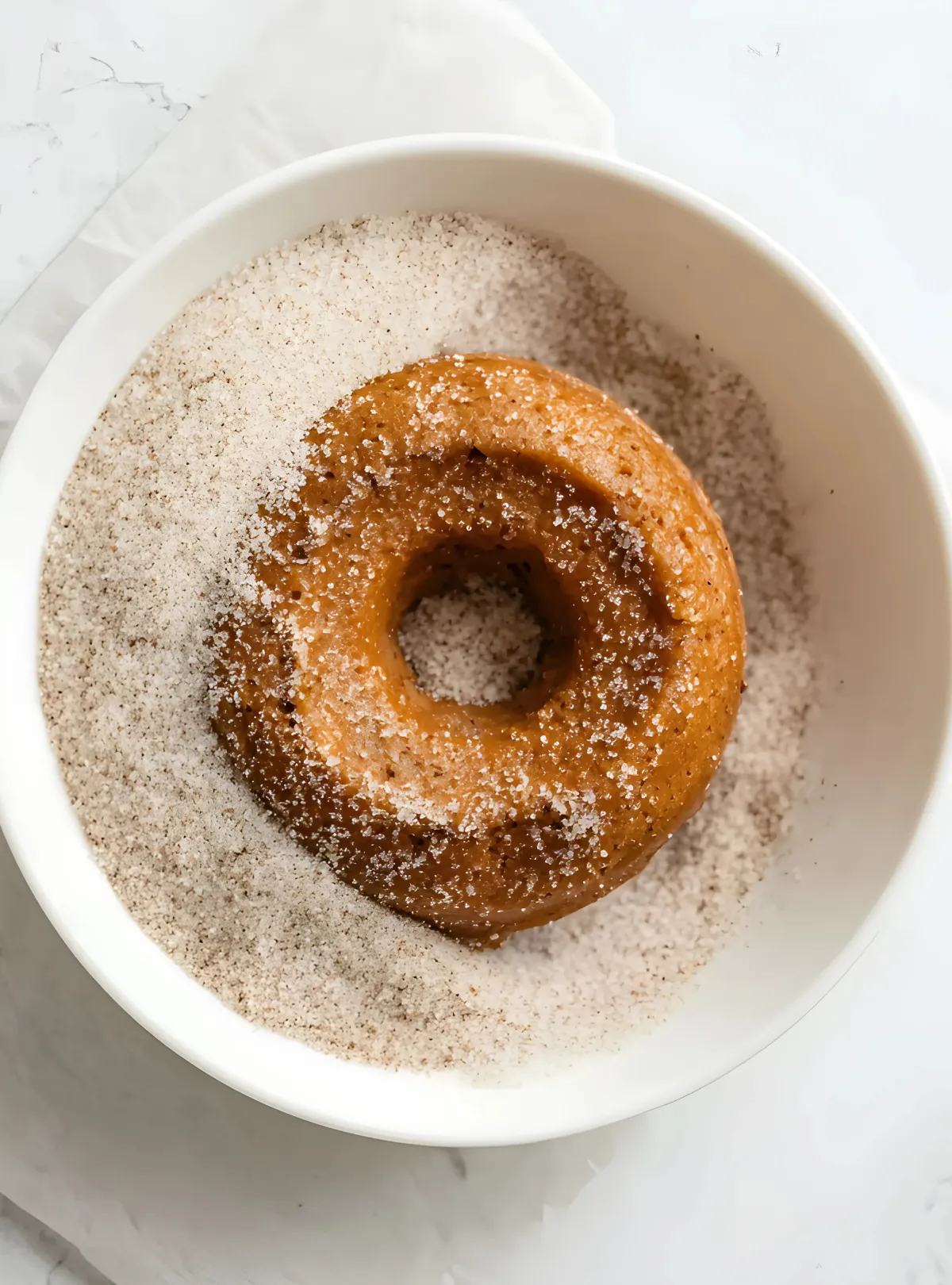 Single donut being coated in cinnamon sugar mixture