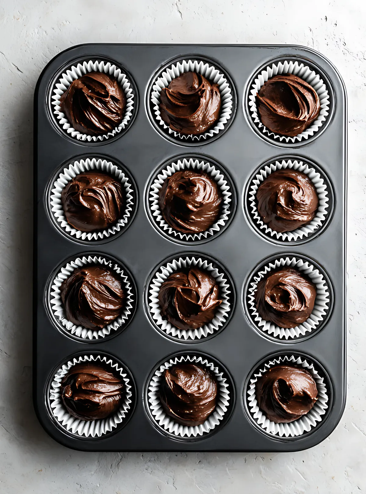 Twelve chocolate cupcakes in muffin tin with chocolate frosting
