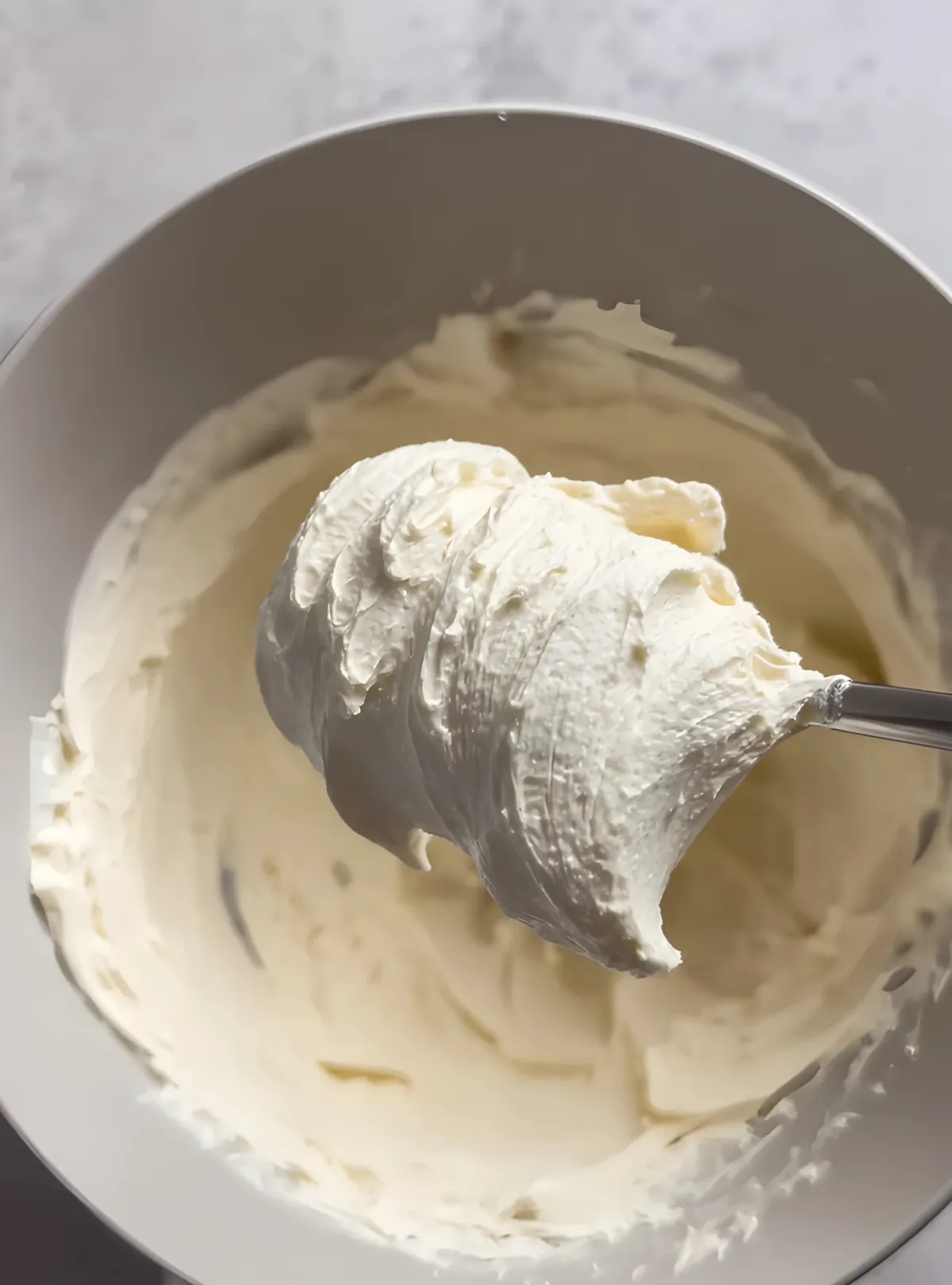 White cream cheese frosting in mixing bowl with spatula