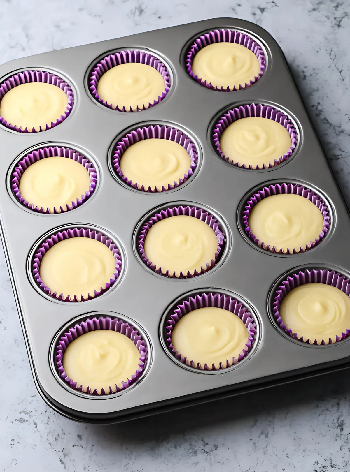 Yellow cupcake batter poured over Oreos in purple liners